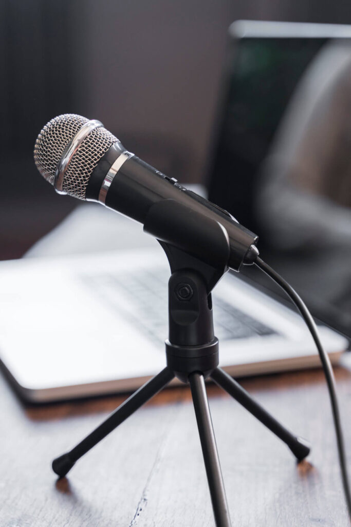 Un microphone noir sur trépied posé sur une table en bois, avec un câble connecté. En arrière-plan, un ordinateur portable flou est visible.